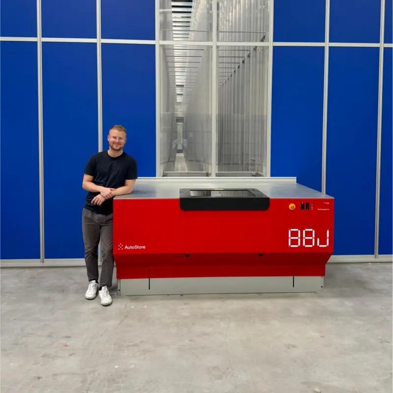 Man standing beside red AutoStore warehouse robot