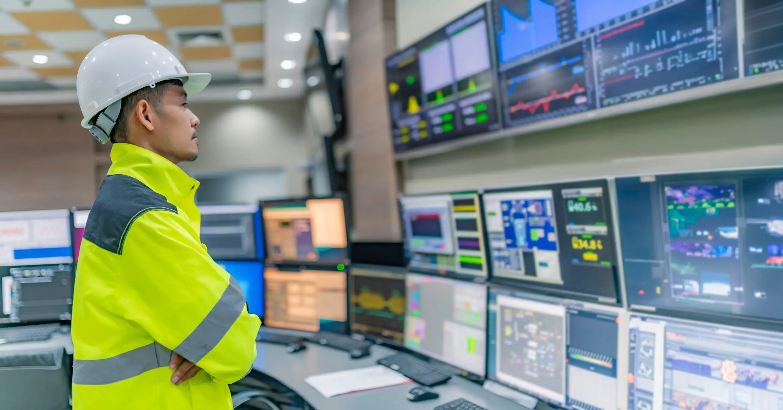 Engineer monitoring multiple computer screens in control room.
