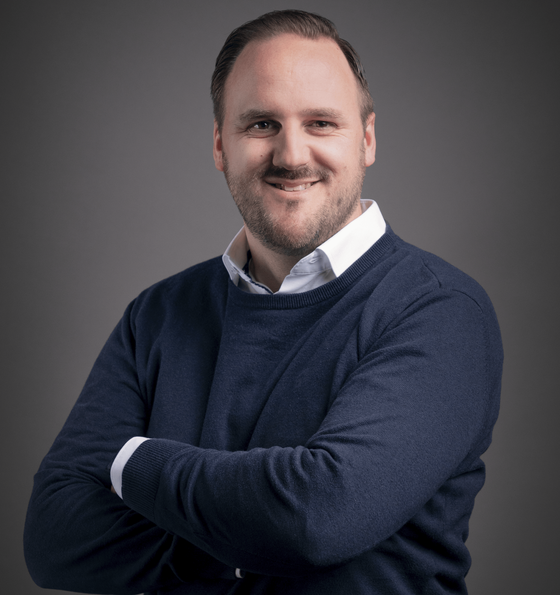 Smiling man in blue sweater folds arms.