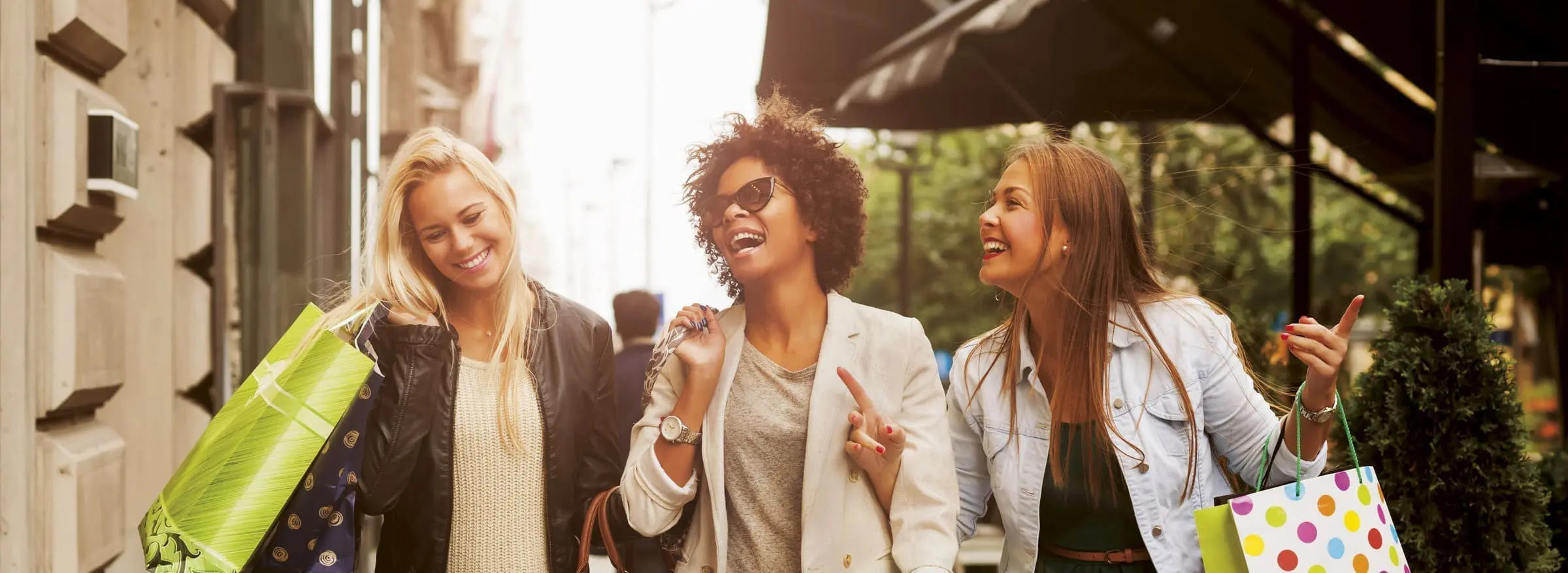 Three women laughing with shopping bags outdoors.