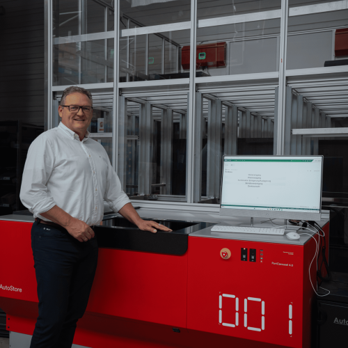 Man standing by AutoStore red robot system in warehouse.